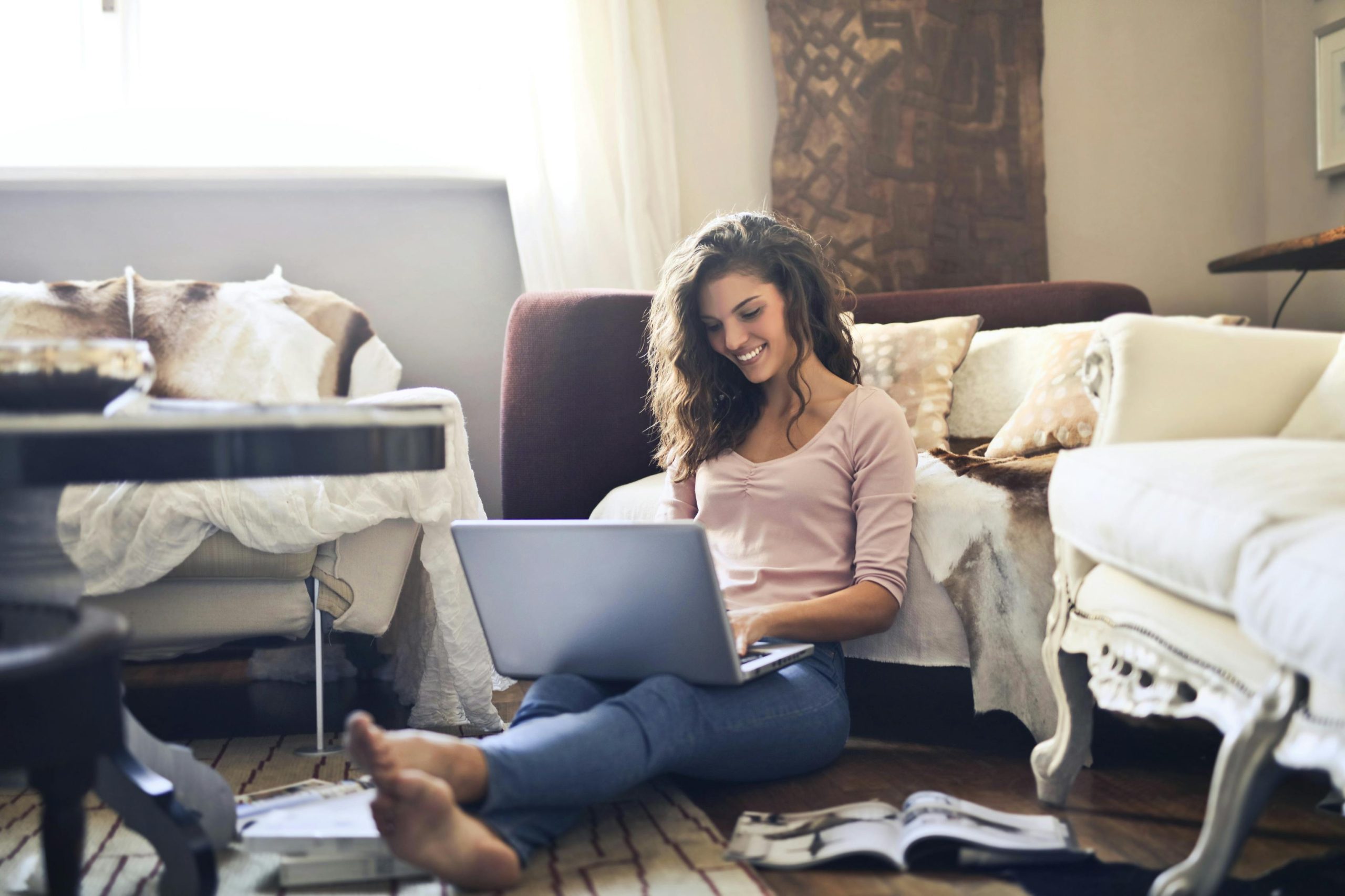 Smiling woman using a laptop seated on the floor in a cozy living room, working remotely.