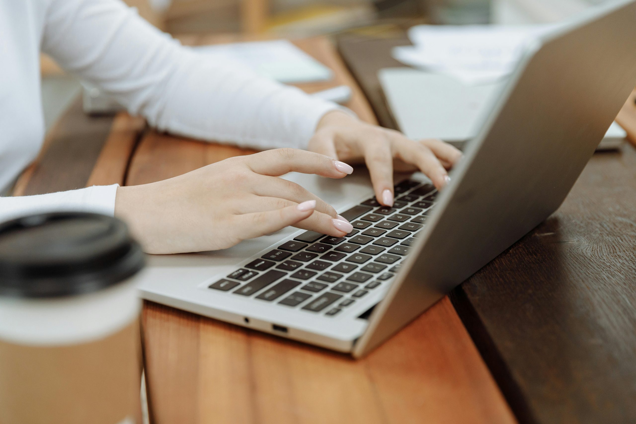 Close-up of a woman's hands typing on a laptop next to a coffee cup in a casual setting.